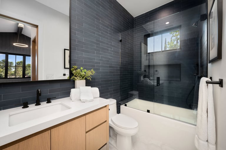 Modern bathroom interior with sleek design featuring glass shower, white vanity, and black tile walls